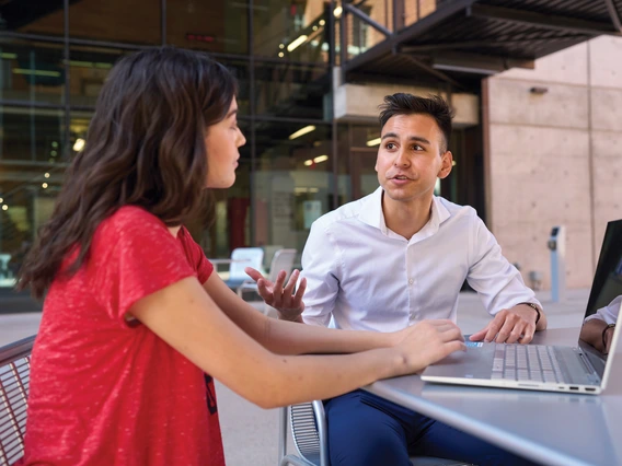 A student and academic advisor sitting outside with a laptop.