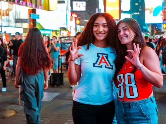 Two students standing in NYC making U of A Wildcat gesture.