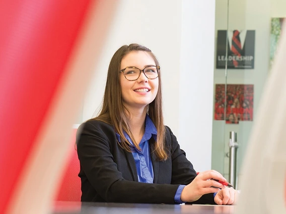 A student in professional attire sitting in a boardroom.