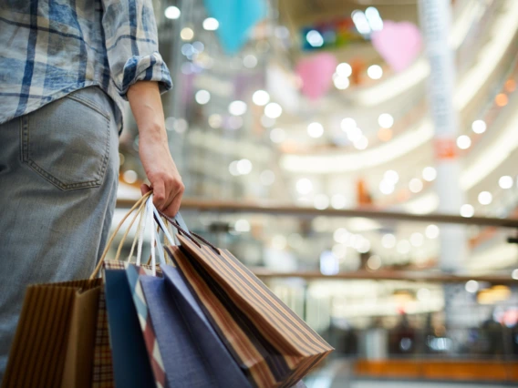 A woman stands in a mall holding shopping bags
