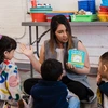 A teacher reads a board book to a group of young children