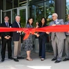 A group of people in front of a building cutting a big red ribbon with giant scissors.
