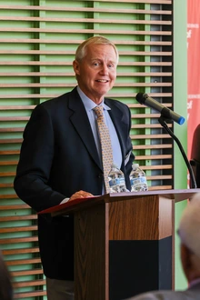 A person stands at the podium, in front of a microphone, speaking to a crowd.